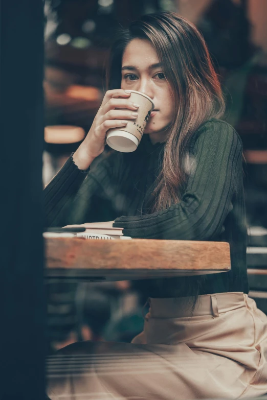 a woman sitting at a table with a cup of coffee, a picture, inspired by Elsa Bleda, trending on unsplash, renaissance, young asian woman, wearing a dark sweater, super high resolution, multiple stories