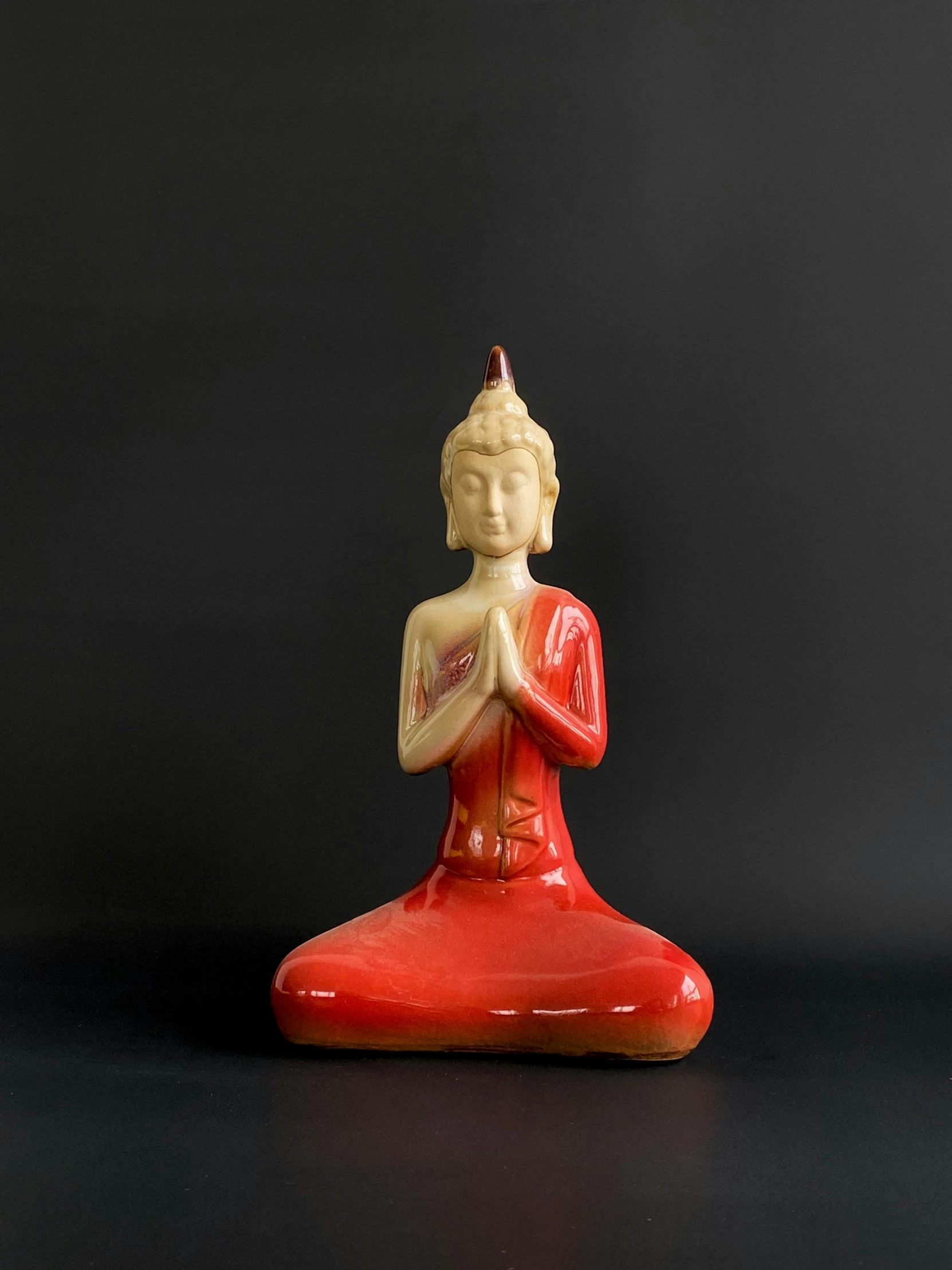 a red buddha figurine sitting on a black surface, by Glennray Tutor, fine art, cream, candle, glazed ceramic, demur