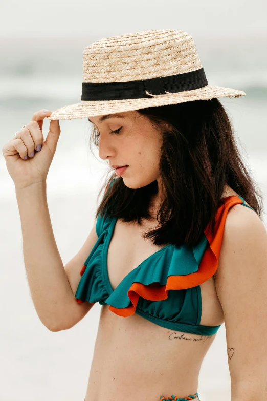 a woman standing on top of a beach next to the ocean, green hat, teal orange, ruffles, bralette