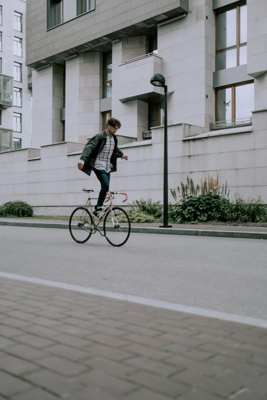 a man riding a bike down a street next to tall buildings, pexels contest winner, helsinki, gif, teenage boy, square