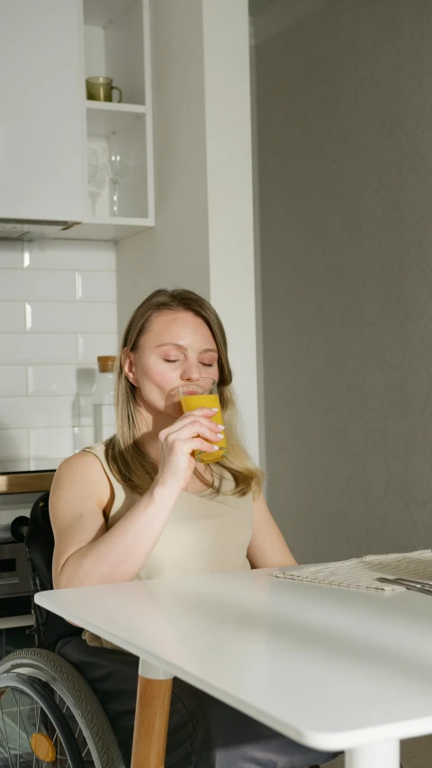 a woman in a wheelchair drinking from a cup, pexels, hyperrealism, wearing yellow croptop, on kitchen table, blonde swedish woman, high quality photo