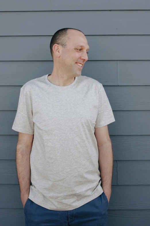 a man standing in front of a gray wall, wearing a t-shirt, dan volbert, wear's beige shirt, profile image