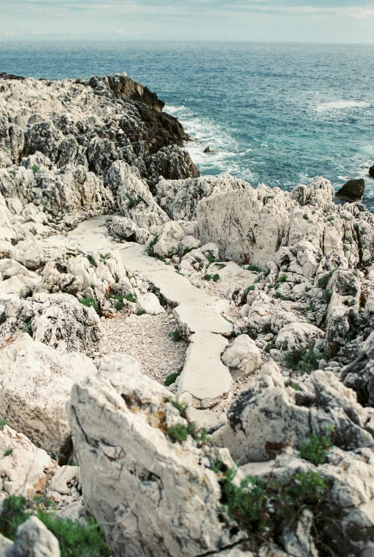 a man standing on top of a rocky cliff next to the ocean, by Coppo di Marcovaldo, stone paths, bleached colors, small steps leading down, top - down photograph