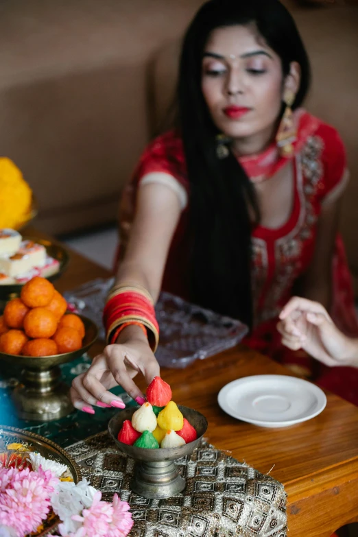 a woman sitting at a table with a plate of food, colorful adornments, hindu aesthetic, candy decorations, sf