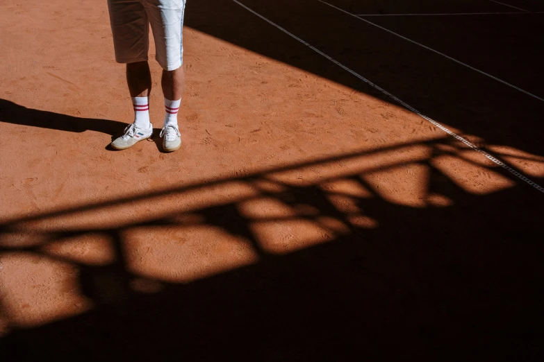 a man standing on a tennis court holding a racquet, inspired by Hans Mertens, pexels contest winner, long cast shadows, terracotta, wearing white sneakers, 15081959 21121991 01012000 4k