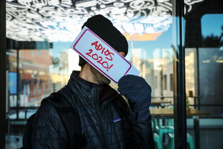 a man holding a sign in front of a building, by Alejandro Obregón, trending on unsplash, graffiti, visor covering eyes, looking through frosted glass, 2 0 2 2 picture of the year, adhd