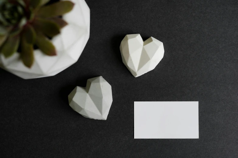 a couple of paper hearts sitting on top of a table, a marble sculpture, inspired by Robert Mapplethorpe, crystal cubism, business card, white concrete, slate, miniature product photo