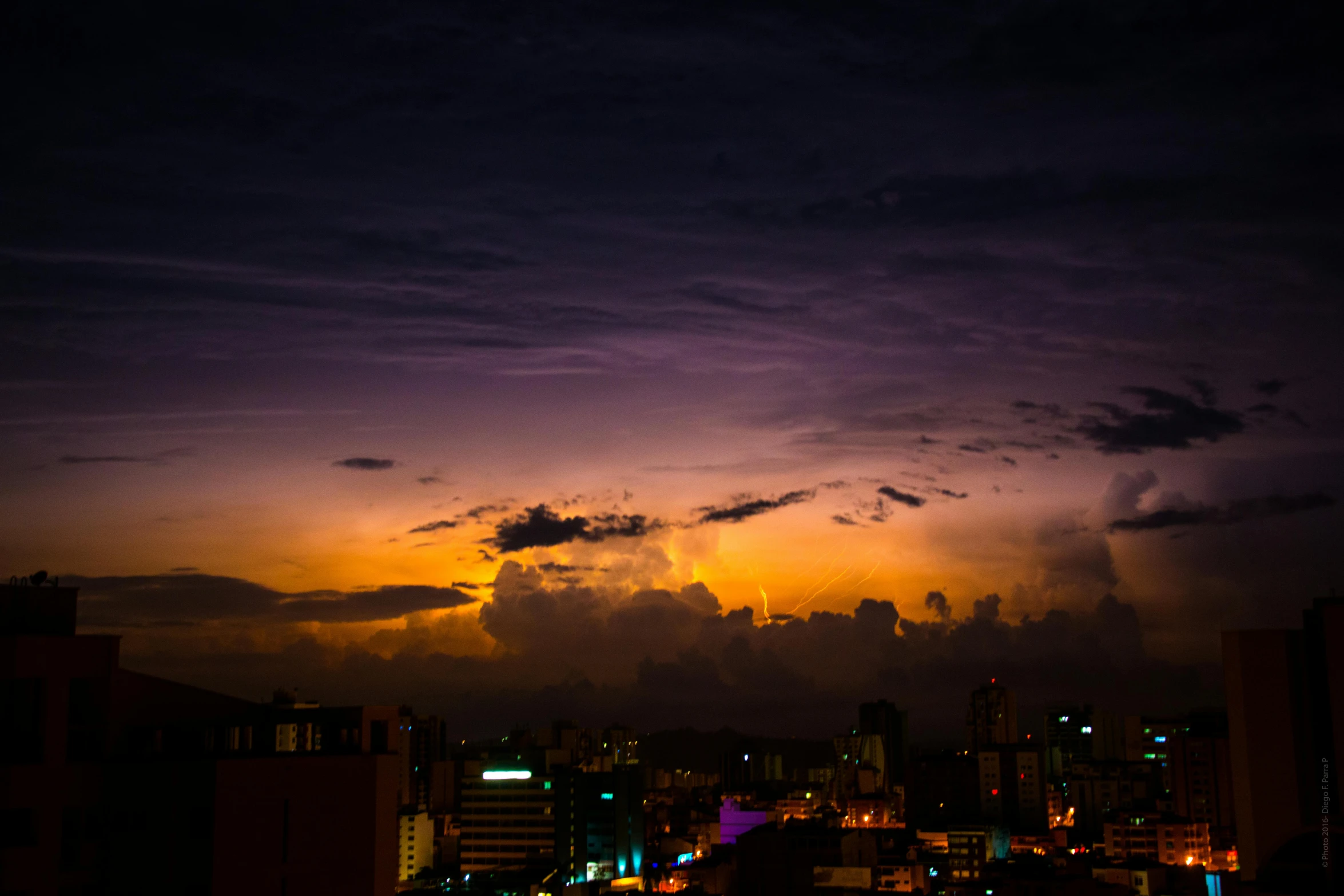 a view of a city at night from a high rise building, by Niklaus Manuel, pexels contest winner, hurufiyya, sun after a storm, colombo sri lanka cityscape, violet and yellow sunset, thunderclouds in the sky