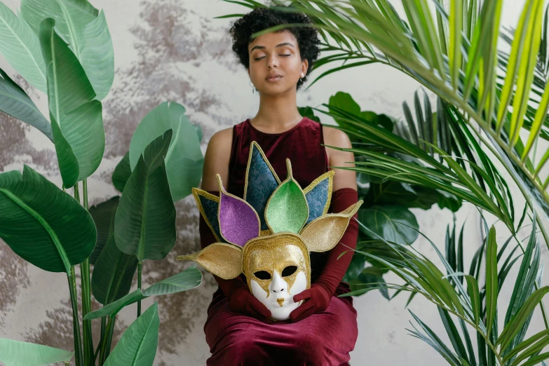 a woman sitting on a chair with a mask on her head, inspired by Leonora Carrington, trending on pexels, afrofuturism, woman made of plants, crown made of felt, multicoloured, diverse costumes