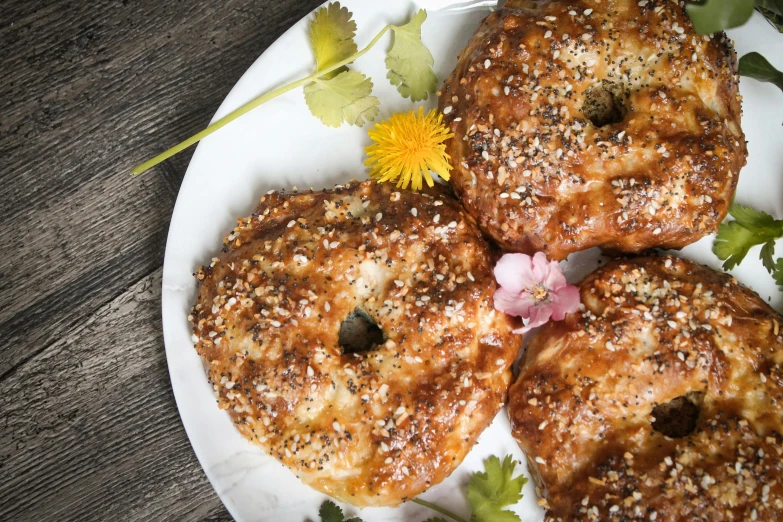 a white plate topped with three donuts on top of a wooden table, by Caroline Mytinger, hurufiyya, with bread in the slots, luscious patty with sesame seeds, flowers, bagels