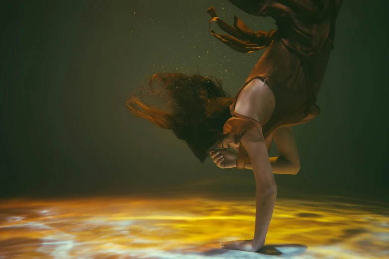 a woman is doing a handstand in the water, an album cover, inspired by Brooke Shaden, pexels contest winner, takato yomamoto. 4 k, brown, liquid gold, volumetric underwater lighting