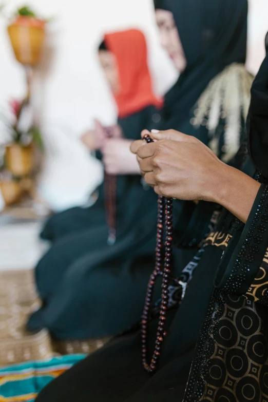 a group of women sitting on top of a floor, by Maryam Hashemi, trending on unsplash, hurufiyya, holding a holy symbol, beads, wearing black silk robe, hands pressed together in bow