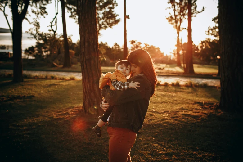 a woman holding a child in a park, pexels contest winner, warm golden backlit, avatar image, high quality image, handsome