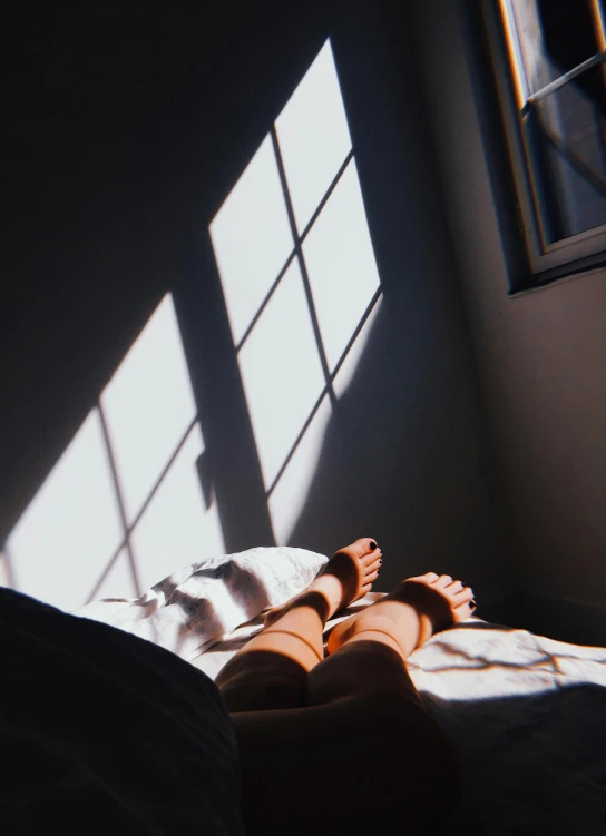 a person laying on a bed in front of a window, inspired by Elsa Bleda, light and space, trending on vsco, volumetric sunlight, legs visible, taken in the late 2000s