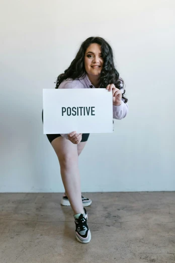 a woman holding a sign that says positive, by Olivia Peguero, full body posing, promo image, pokimane, plus-sized