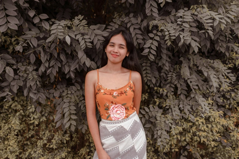 a woman posing for a picture in front of a bush, pexels contest winner, realism, wearing a tanktop and skirt, batik, background image, portait photo profile picture