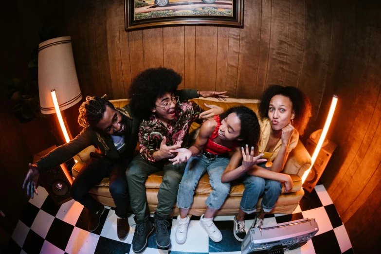 a group of people sitting on top of a couch, a portrait, by Washington Allston, pexels contest winner, funk art, long afro hair, shot with a camera flash, annoying sister vibes, a high angle shot