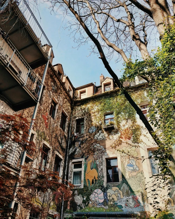 a building with a mural on the side of it, a photo, pexels contest winner, lots of foliage, kreuzberg, old color photo, conde nast traveler photo