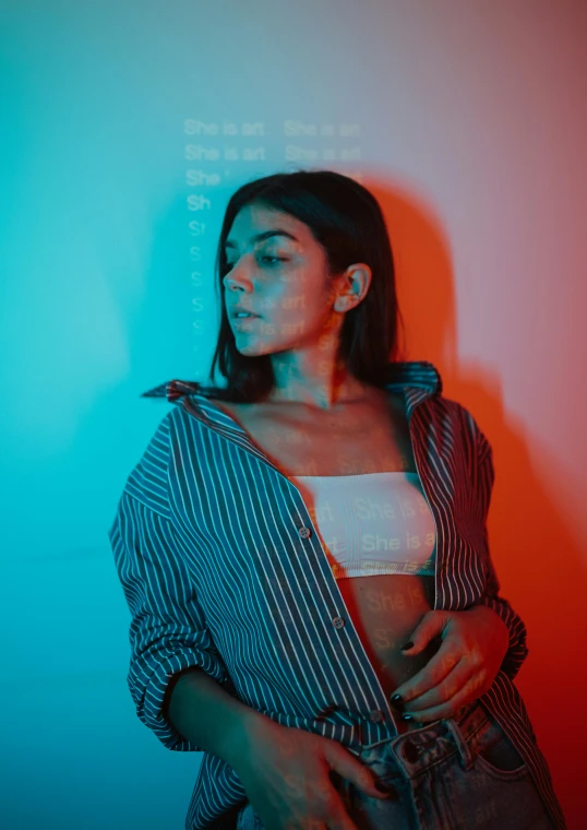 a woman standing in front of a blue and red wall, an album cover, inspired by Elsa Bleda, pexels contest winner, holography, wearing stripe shirt, profile image, madison beer, in dark room