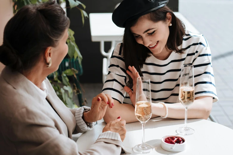 two women sitting at a table with wine glasses, trending on pexels, wearing a french beret, painted nails, charcoal and champagne, striped