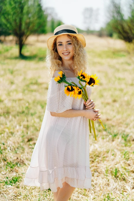 a woman standing in a field holding a bunch of sunflowers, a picture, shutterstock, romanticism, pale skin curly blond hair, square, happy fashion model, with hat