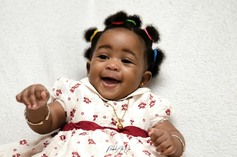 a close up of a baby wearing a dress, by Chinwe Chukwuogo-Roy, pexels contest winner, playful smile, two pigtails hairstyle, wears a egyptian ankh necklace, high resolution product photo