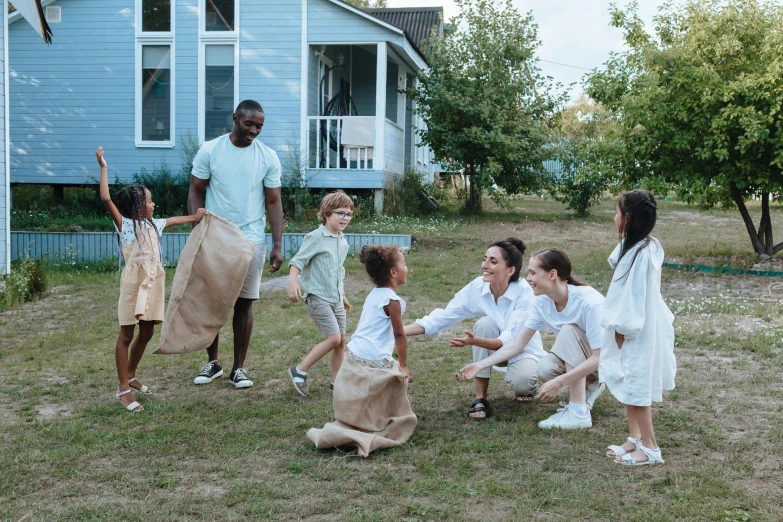 a group of people that are standing in the grass, families playing, wearing a linen shirt, at home, bags on ground