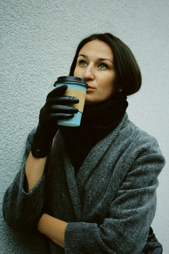 a woman wearing gloves holding a cup of coffee, wearing a turtleneck and jacket, blue-black, warsaw, ekaterina
