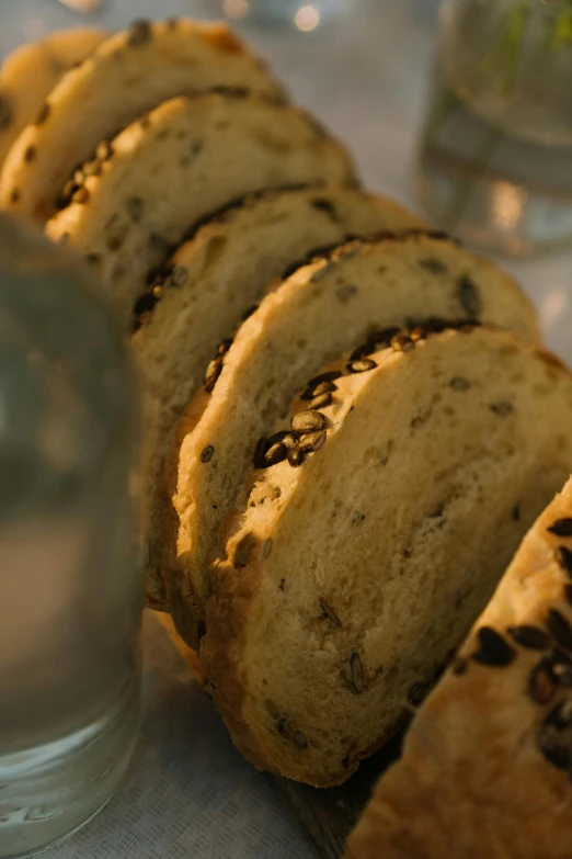 a loaf of bread sitting on top of a table next to a glass of water, soft evening lighting, seeds, rack, holiday