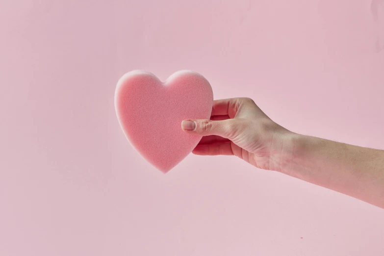 a person holding a pink heart in their hand, foam, textured base ; product photos, super smooth, blobs