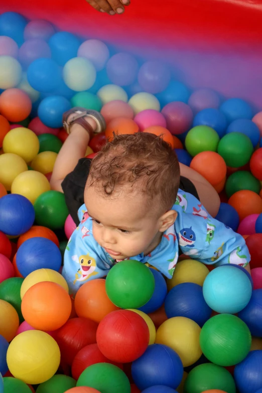 a baby is playing in a ball pit, looking towards the camera, multicoloured, square, feature