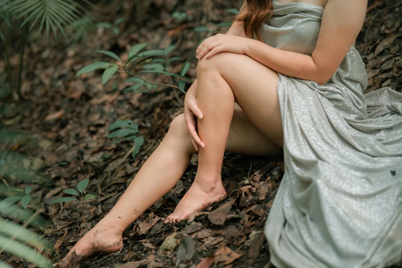 a woman in a silver dress sitting on the ground, trending on pexels, australian tonalism, swollen veins, in forest, paradise garden massage, thigh skin