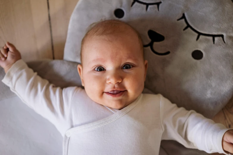 a baby laying on top of a bed next to a stuffed animal, pexels contest winner, happening, smiling down from above, close up face detail, grey, caspar david