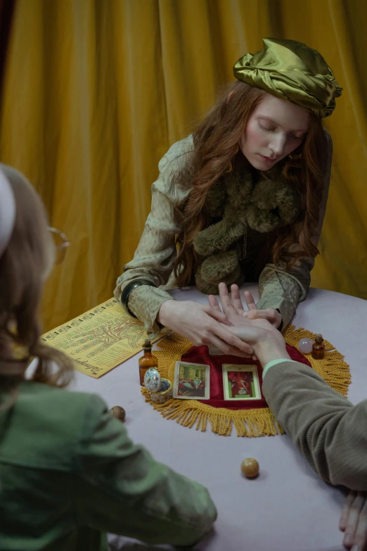 a group of people sitting around a table, by Wes Anderson, unsplash, renaissance, fortune teller, eleanor tomlinson, tarot design, ignant