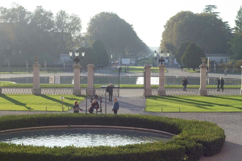 a group of people sitting around a fountain in a park, gate, aqueducts, morning lighting, distant photo