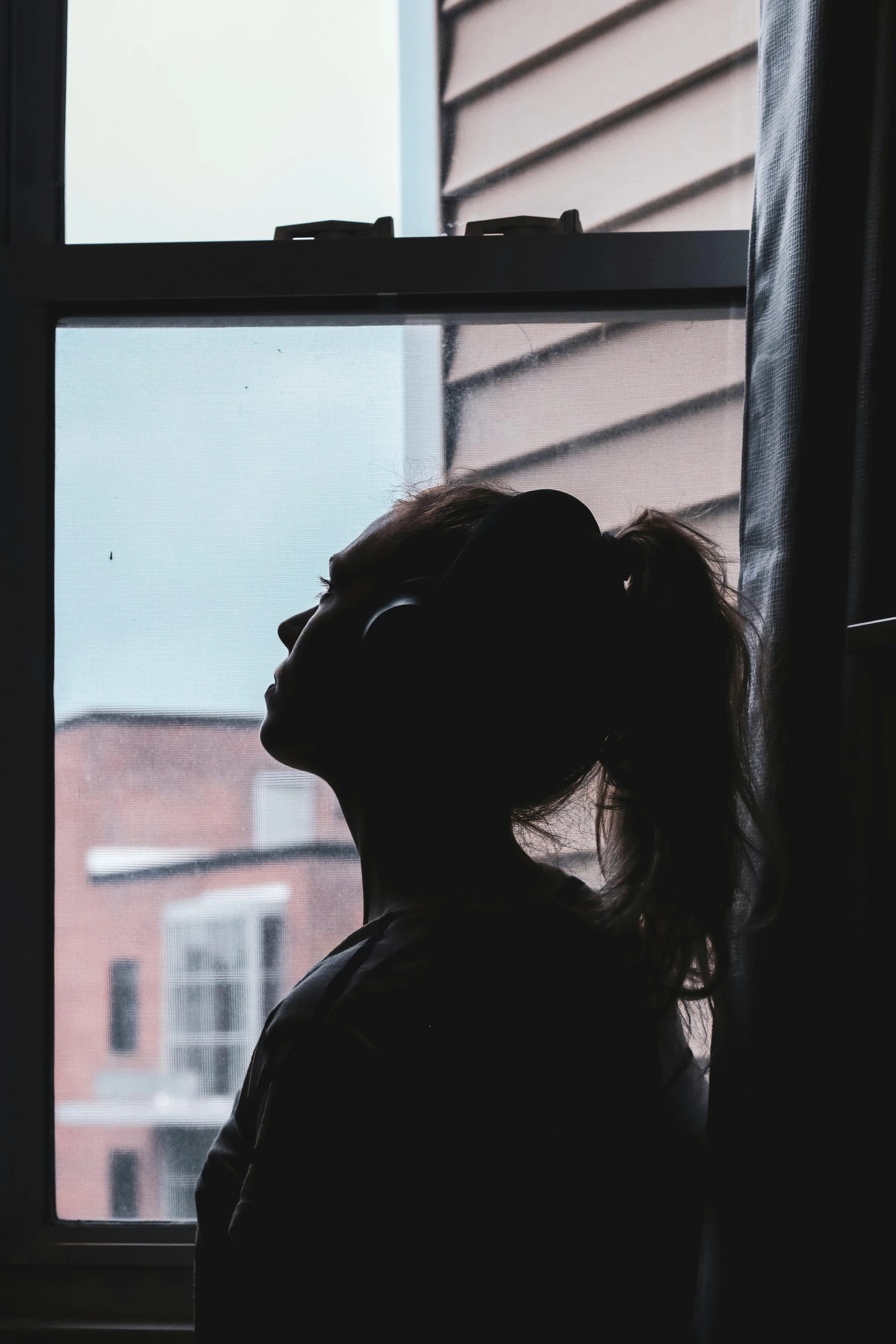 a silhouette of a woman looking out a window, trending on pexels, sad sky, instagram post, backlit ears, queer woman