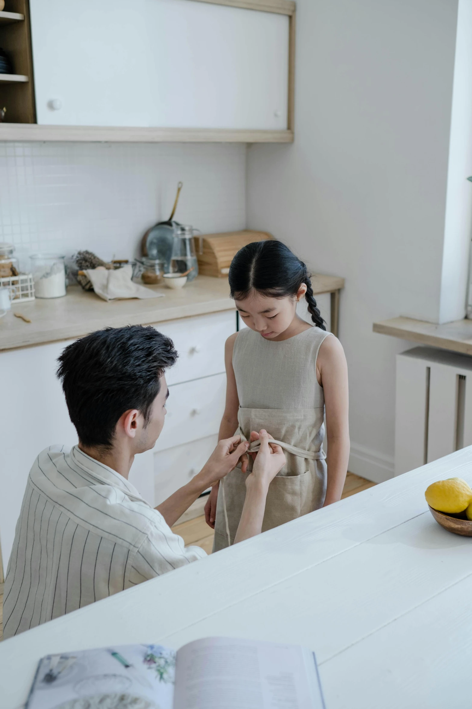 a man standing next to a woman in a kitchen, pexels contest winner, young asian girl, touching her clothes, minimalistic design, kids talking to fruit people