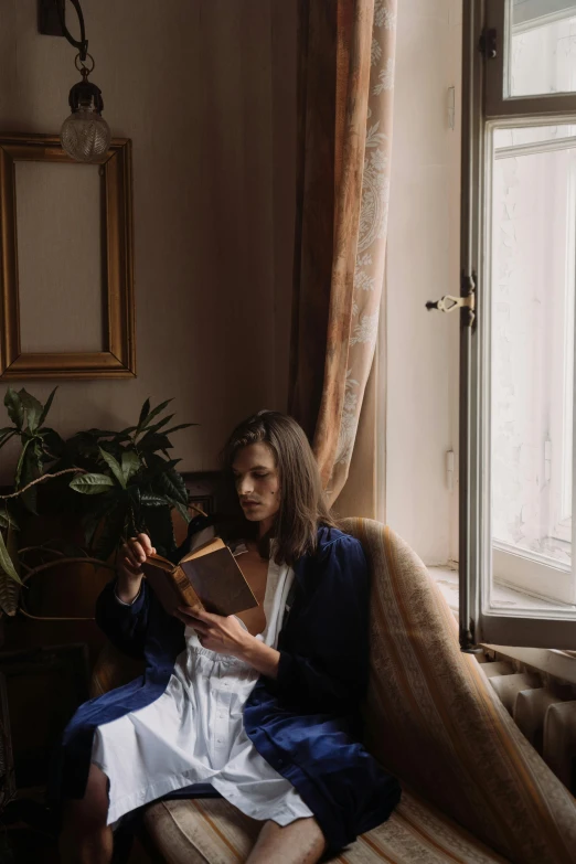 a woman sitting on a couch reading a book, inspired by Balthus, pexels contest winner, renaissance, standing near a window, low quality photo, wearing blue robe, gif