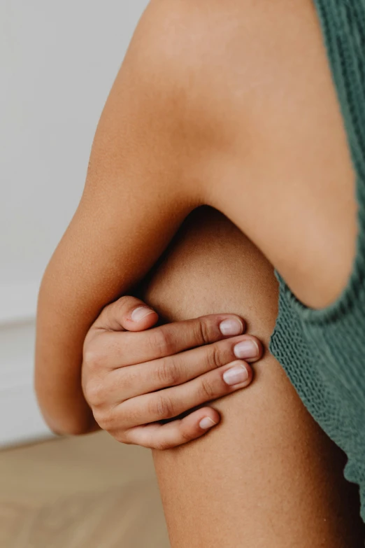 a woman sitting on the floor holding her knee, by Nina Hamnett, trending on pexels, renaissance, closeup of arms, cysts, arms behind back, manuka