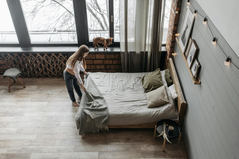a woman standing next to a bed in a bedroom, by Adam Marczyński, pexels contest winner, hardwood floors, interior of a loft, angle view, throw
