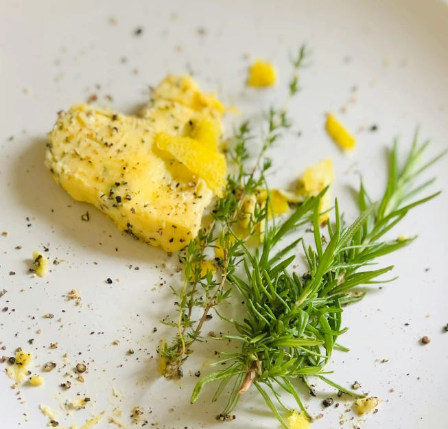 a white plate topped with an omelet and a sprig of rosemary, a picture, unsplash, renaissance, butter sculpture, particles disintegration, herbs, mono-yellow