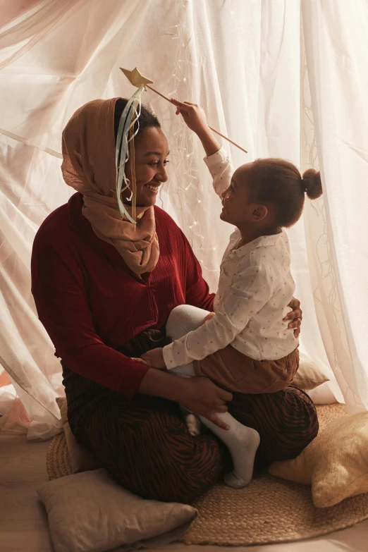 a woman sitting on top of a bed holding a baby, inspired by The Family Circus, pexels contest winner, visual art, hijab, with brown skin, happy kid, promotional image