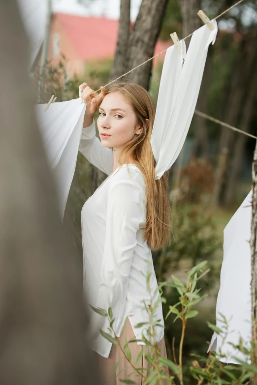 a woman that is standing in the grass, inspired by Konstantin Vasilyev, unsplash, renaissance, white cloth, wearing a white sweater, half - length photo, in a tree