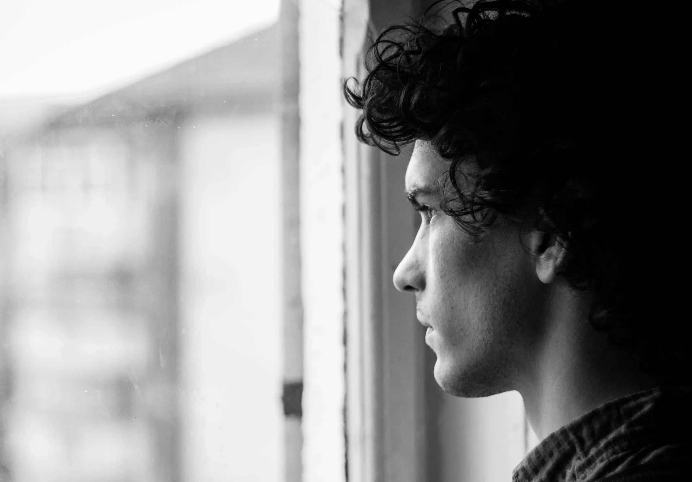 a black and white photo of a man looking out a window, pexels, serial art, finn wolfhard, profile picture 1024px, a handsome man，black short hair, curly haired
