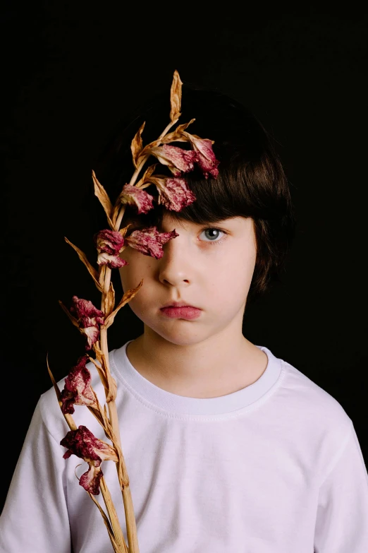 a young boy holding a dried flower in front of his face, an album cover, ((portrait)), non-binary, concerned expression, ignant