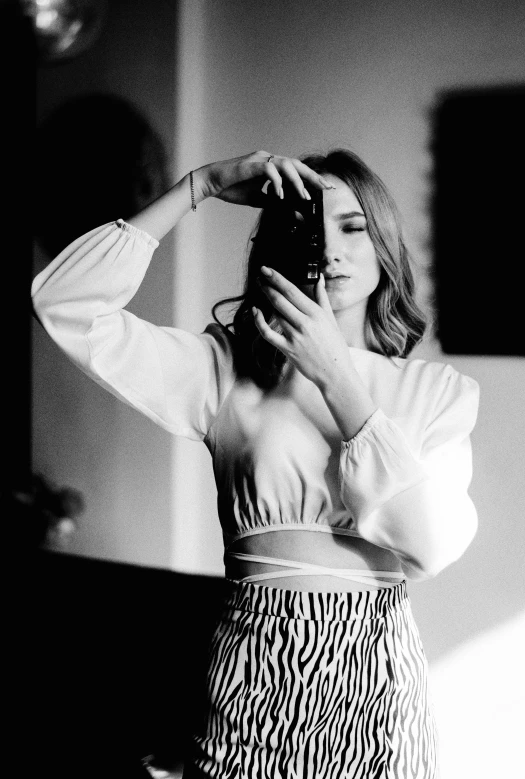 a woman taking a picture of herself in a mirror, a black and white photo, inspired by Emma Andijewska, wearing a cropped top, wearing a white blouse, expressive!!!!!, lilly collins