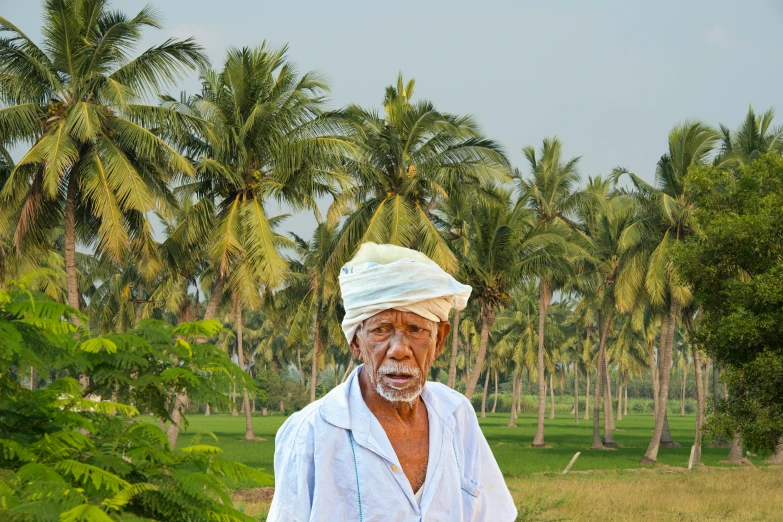 a man standing in a field with palm trees in the background, by Bapu, pexels contest winner, an oldman, avatar image, full color photograph, wearing farm clothes