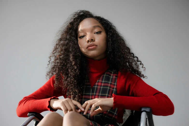 a woman sitting in a chair with her legs crossed, trending on pexels, black teenage girl, wearing a red plaid dress, wearing a red turtleneck sweater, bella poarch