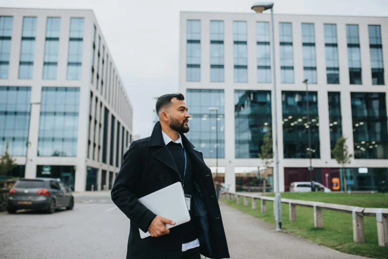 a man with a laptop standing in front of a building, unsplash, coventry city centre, walking to the right, a portrait of rahul kohli, office clothes