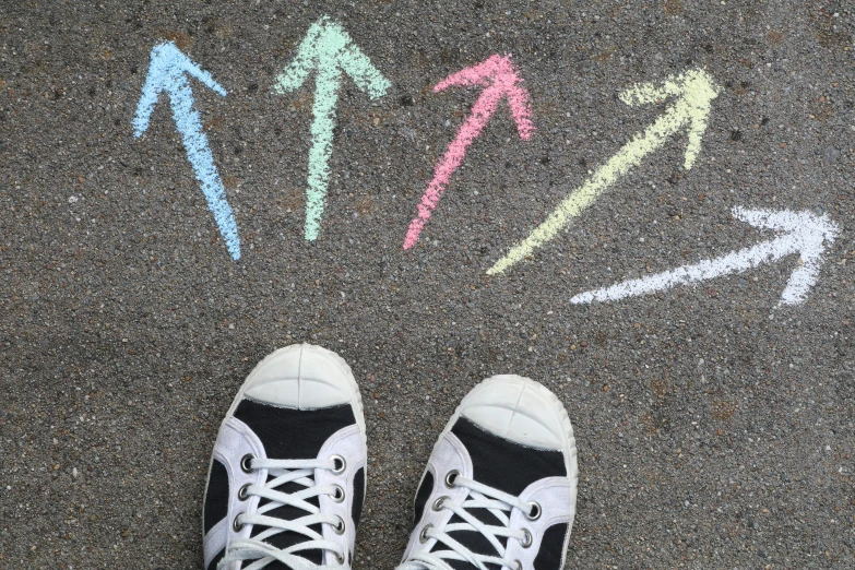 a person standing in front of a chalk drawing of arrows, sneakers, multi - coloured, in a row, top down photo